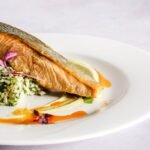 A beautifully plated salmon dish with quinoa, herbs, and a vibrant sauce, perfect for gourmet food lovers.